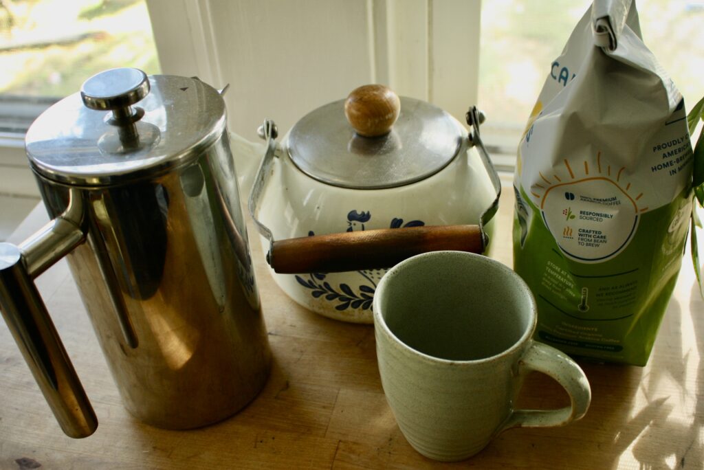 coffee, mug, kettle, bag of coffee, and French press sitting on a table