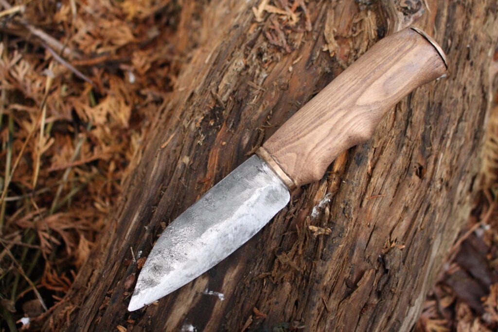 a steel seax knife with a wooden handle and brass fittings sitting on a log