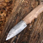 a steel seax knife with a wooden handle and brass fittings sitting on a log