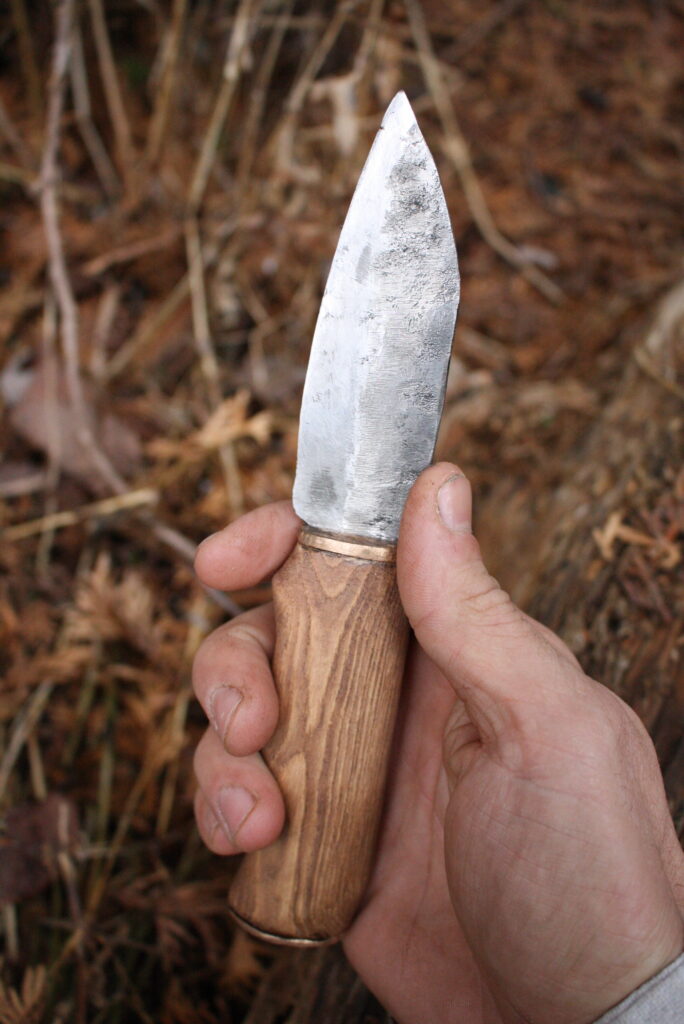 hand holding a single edged steel knife with a wooden handle