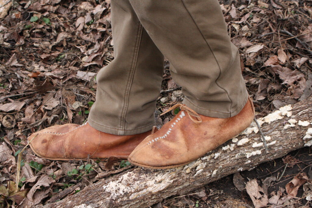 feet wearing soft-soled leather shoes standing on a forest floor 