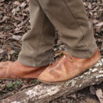 feet wearing soft-soled leather shoes standing on a forest floor