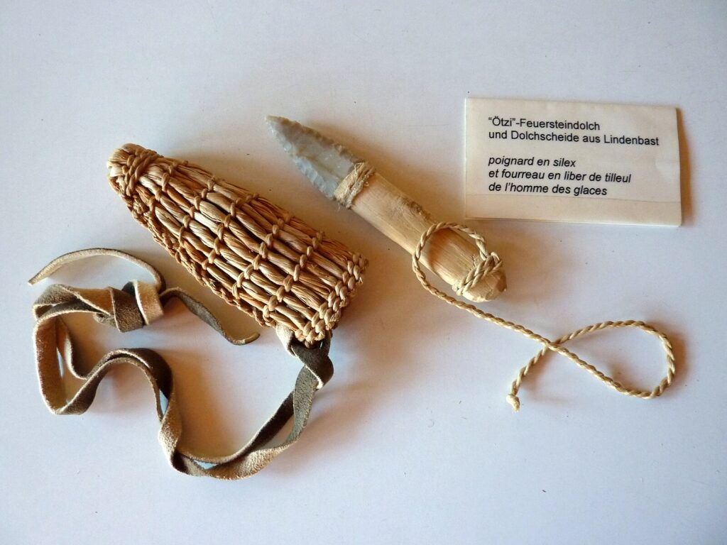 a stone knife with a wooden handle and plant fibre sheath next to a description plaque.