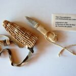 a stone knife with a wooden handle and plant fibre sheath next to a description plaque.