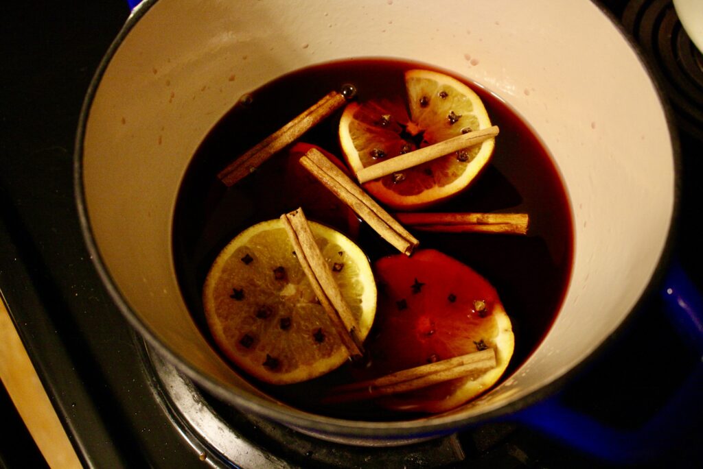 a pot on a stove of mulled wine with orange peals, cinnamon sticks and cloves floating in it.