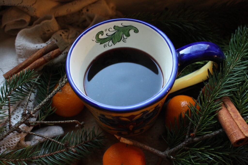 a mug of mulled wine sitting amongst evergreen boughs, oranges and cinnamon sticks.