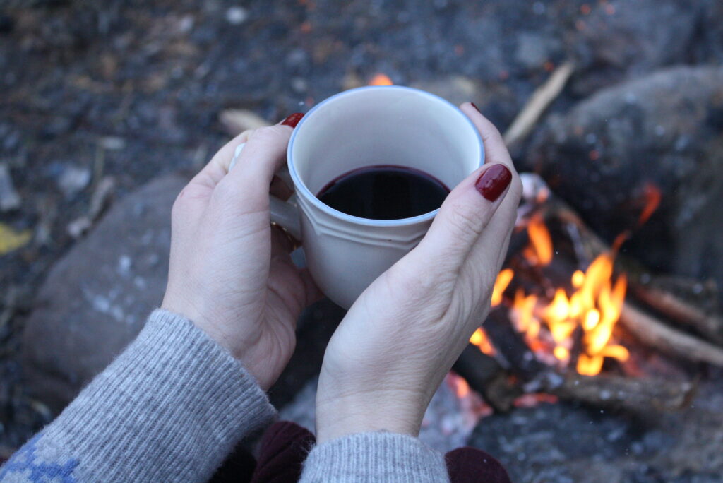 woman's hands holding a a mug in front of a campfire