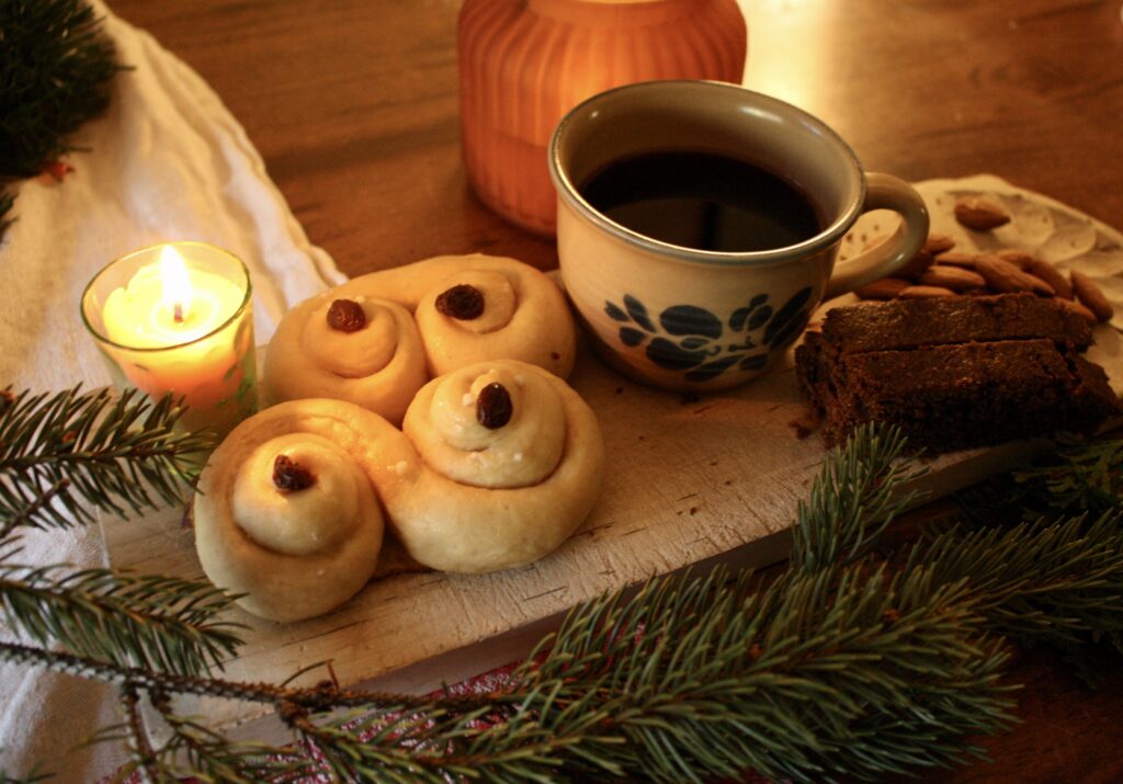 candle, Lucia buns, a mug of mulled wine, ginger bread and almonds on a wooden serving board 