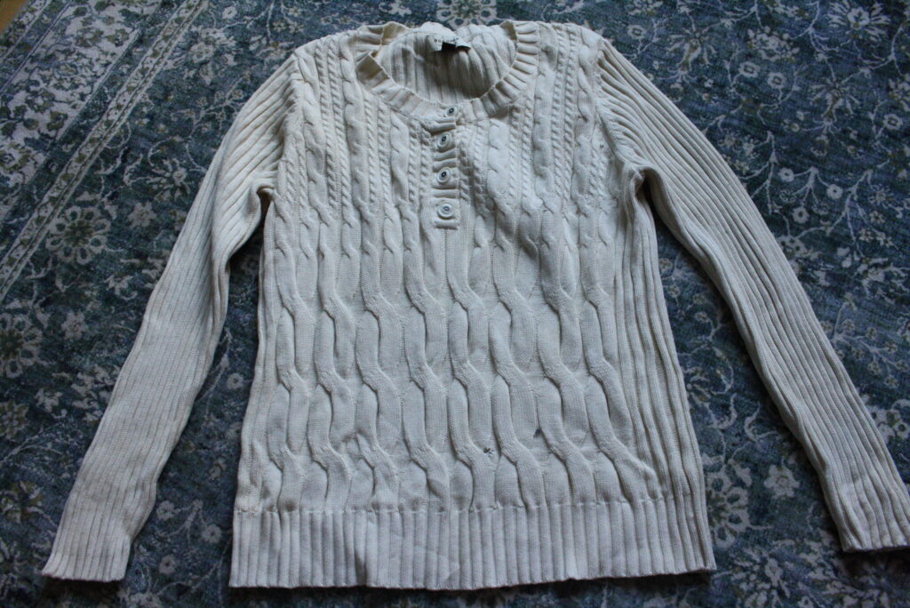 cream, cable knit sweater laying on a blue rug