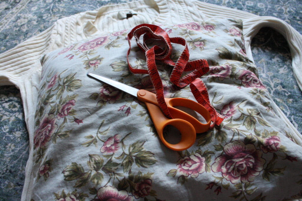 sweater, measuring tape, scissors, and pillow sitting on the floor