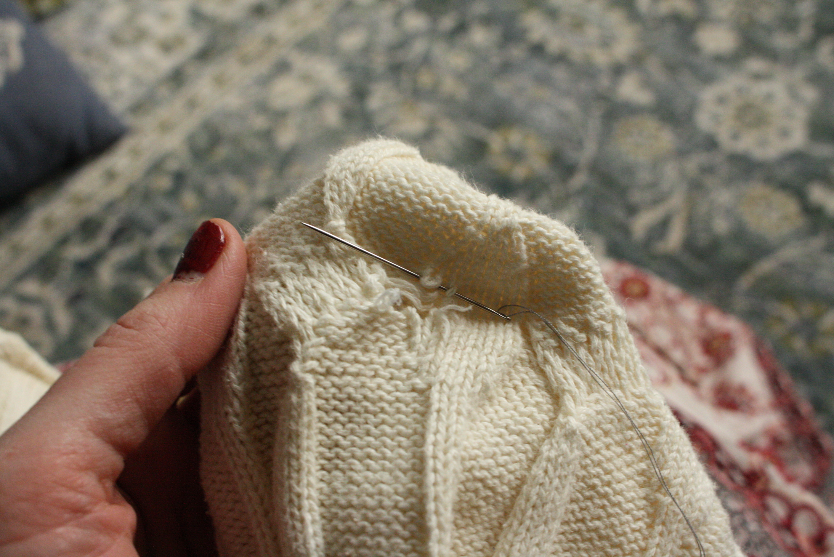 hands sewing a hole in a sweater with a needle and thread