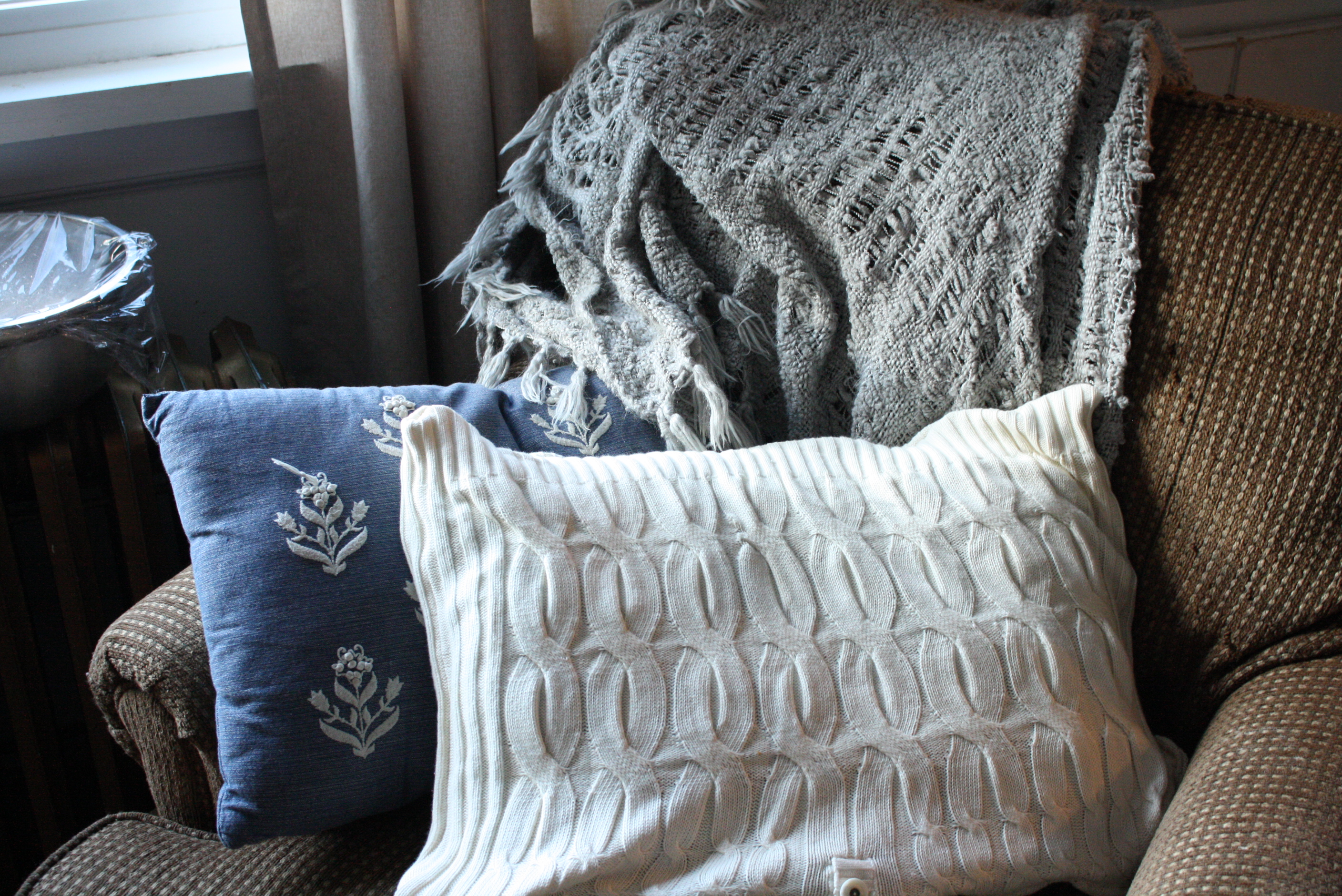 sweater pillow sitting on a brown chair with a grey blanket draped over the back