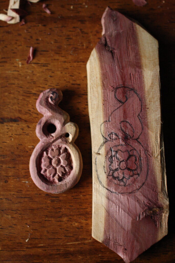 a finished wooden earring sitting next a symmetrical shape of the earring on a piece of wood