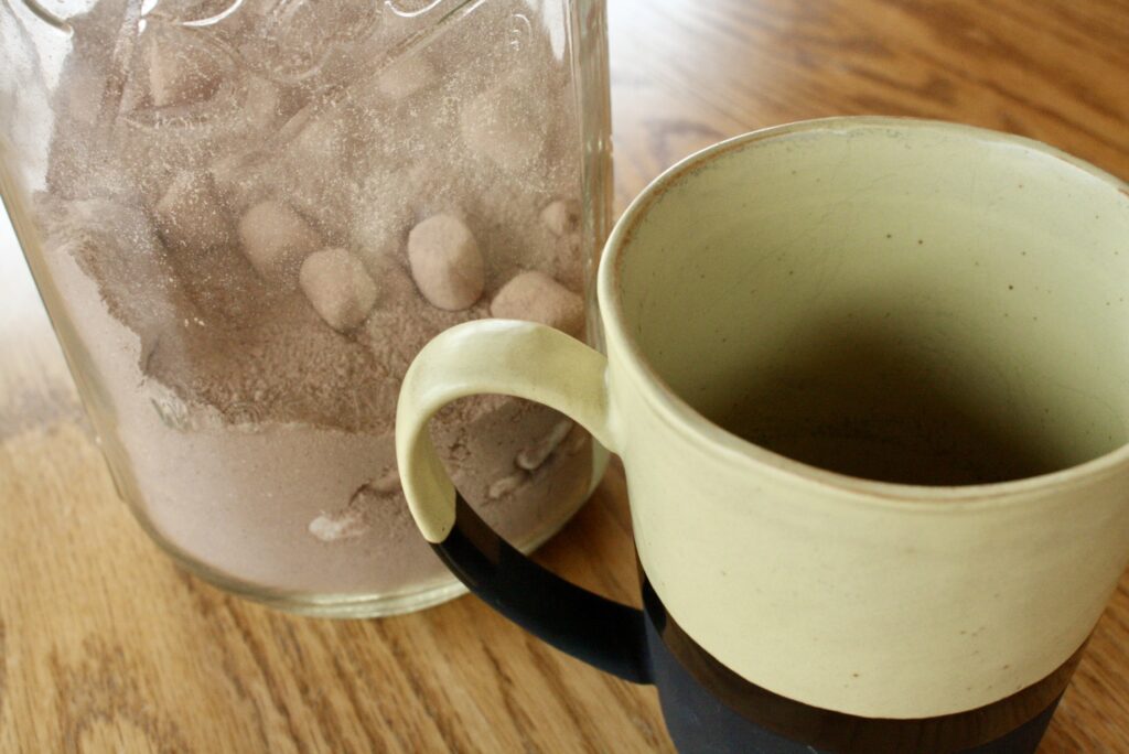 coffee mug sitting beside a powdered hot cocoa mix in a glass jar on a table