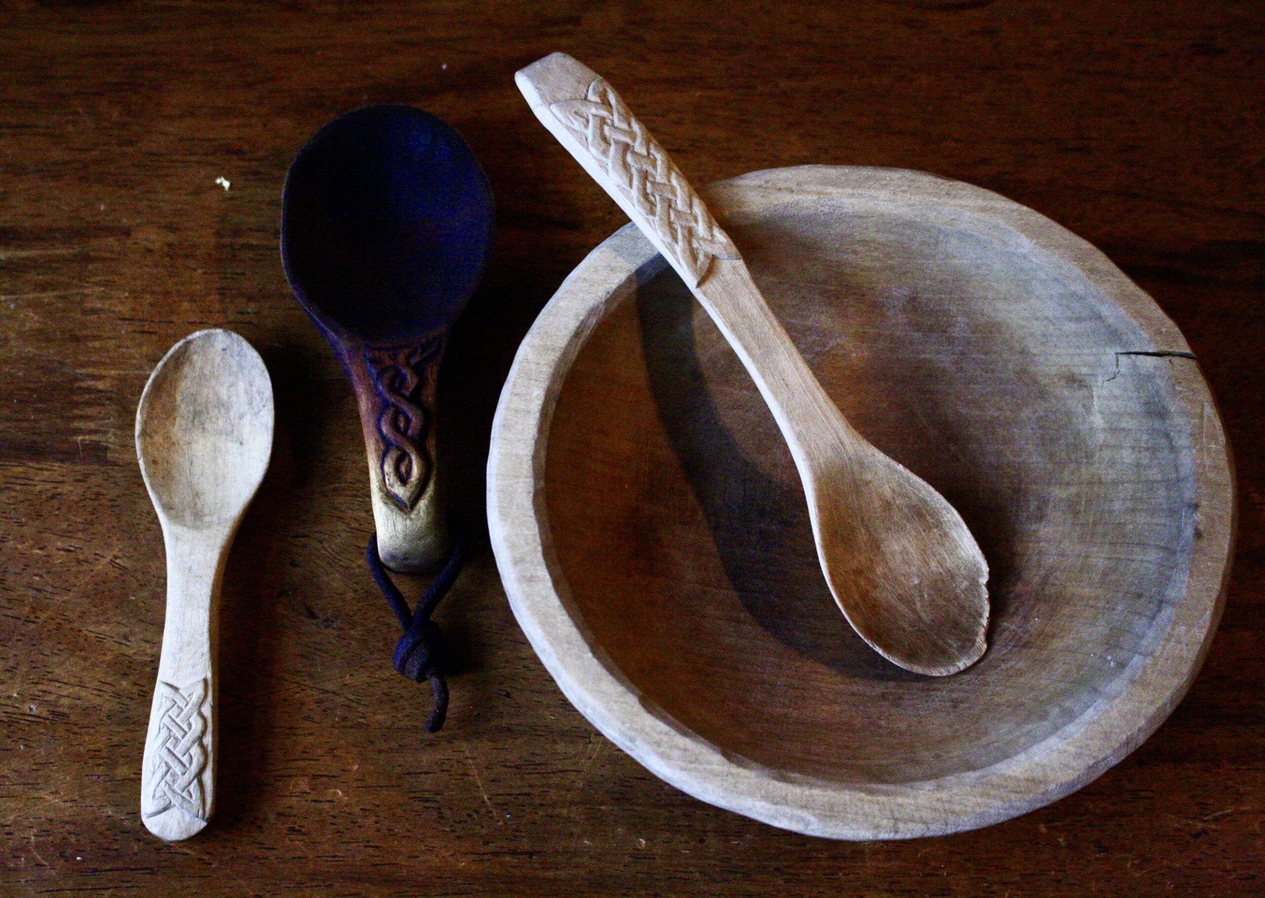 three wooden spoons with folk art knotwork motifs carved on the handles and a wooden bowl sitting on a wooden table top.