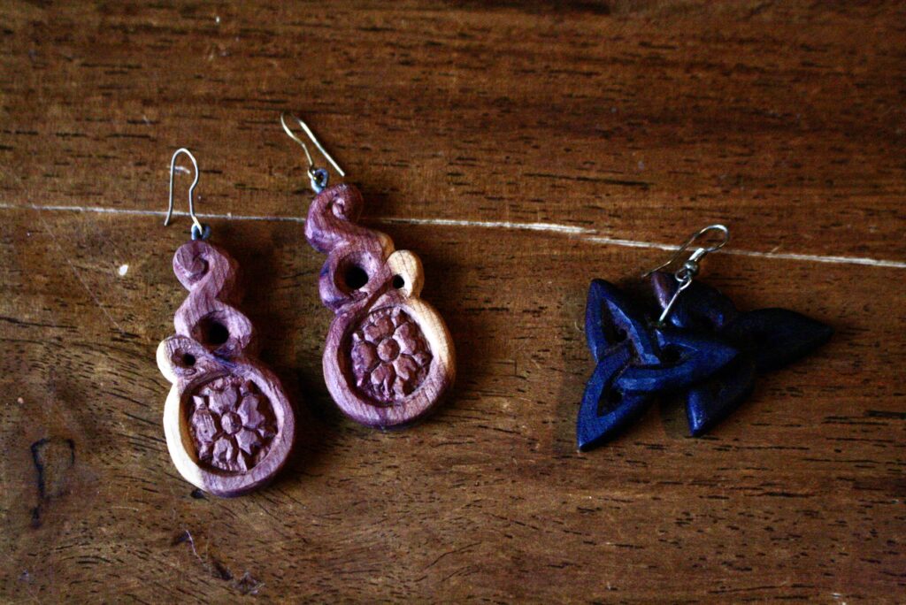 two sets of wooden carved earrings with folk designs sitting on a wooden table