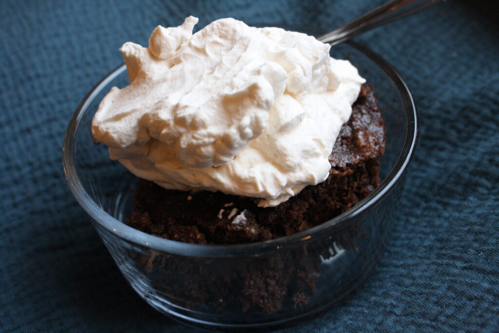 a brownie with whipped cream on top in a small glass bowl