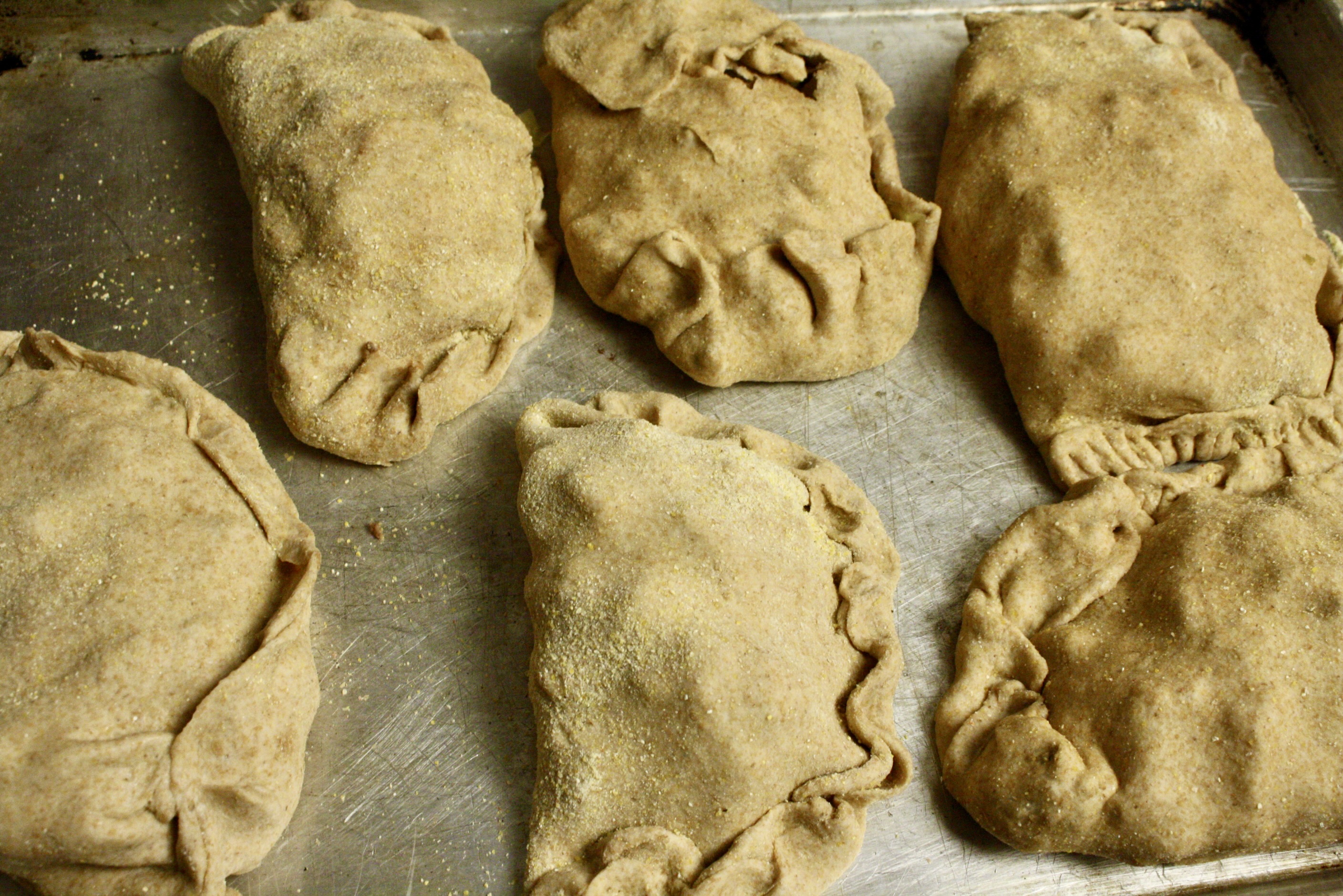 six uncooked pasties on a baking tray