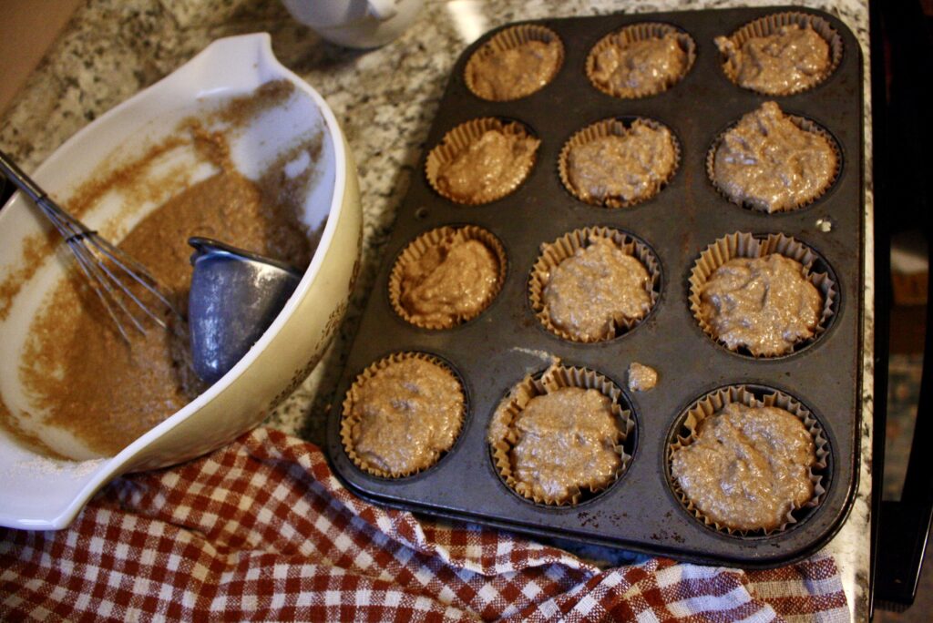 a bowl of muffin batter sitting next to a muffin tin filled with batter