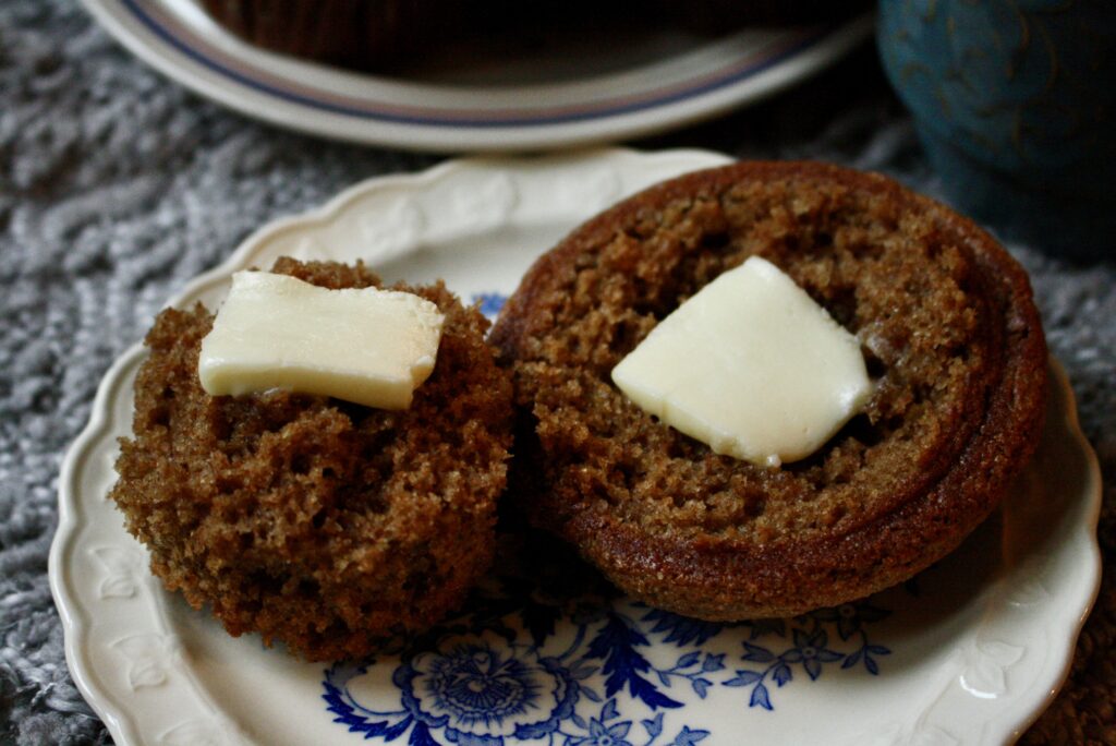 spiced applesauce muffin split in half with melting butter on top of each half on a plate