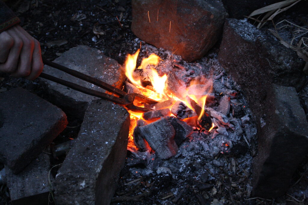 a hand gripping a blacksmith tongs, holding  hot metal in a forge fire.