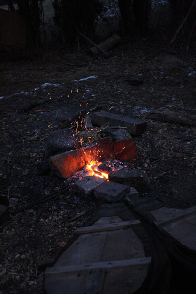 sparks flying in waning daylight from a fire with bellows stoking it