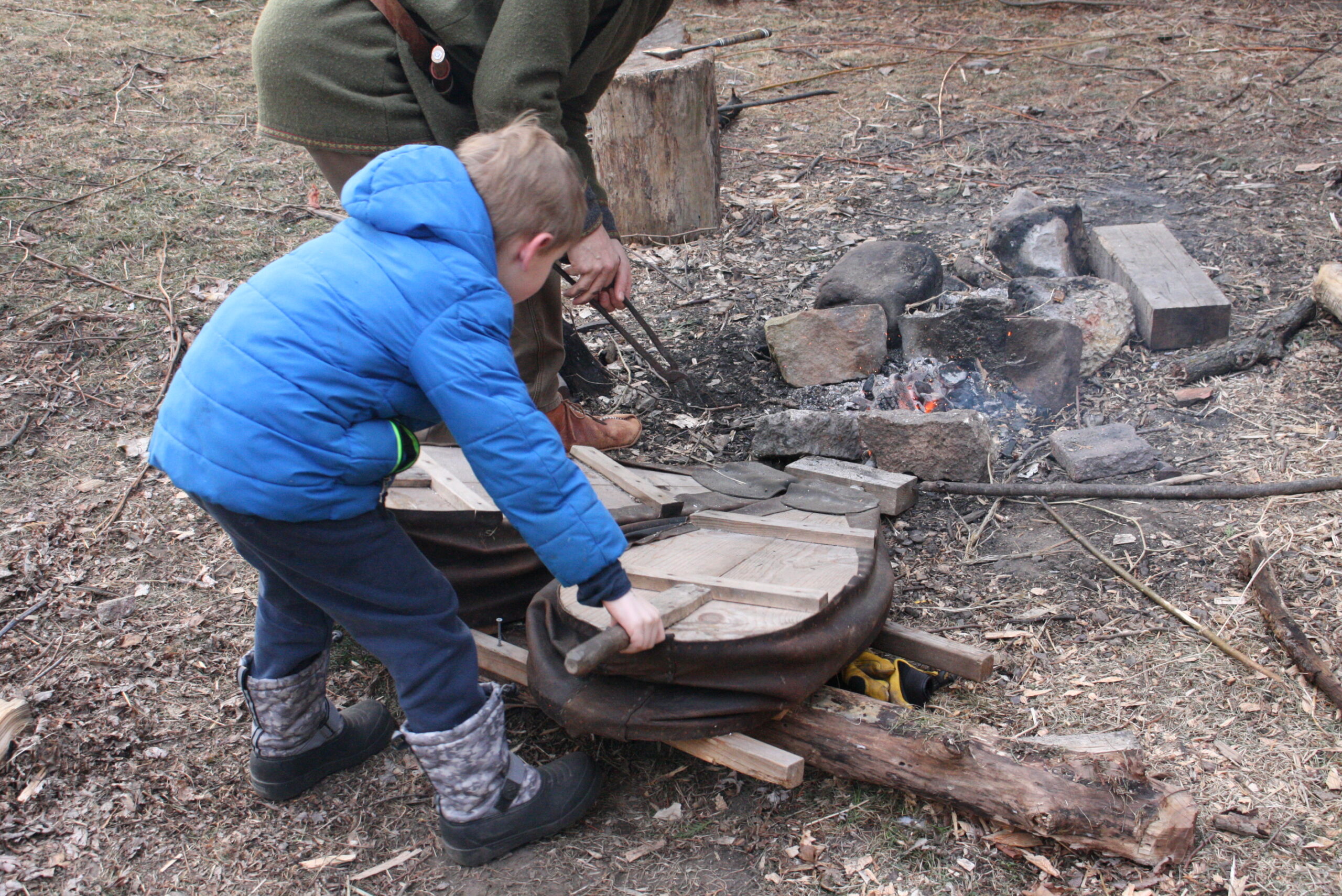 a boy pumping bellows for a backyard forge