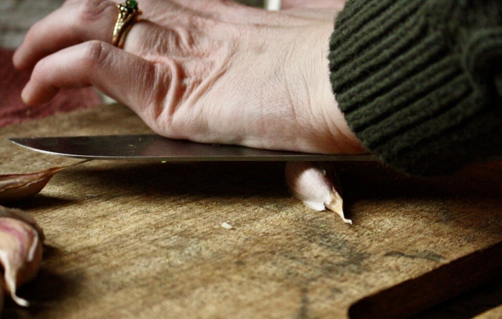 hand using the flat end of a knife to crush a clove of garlic