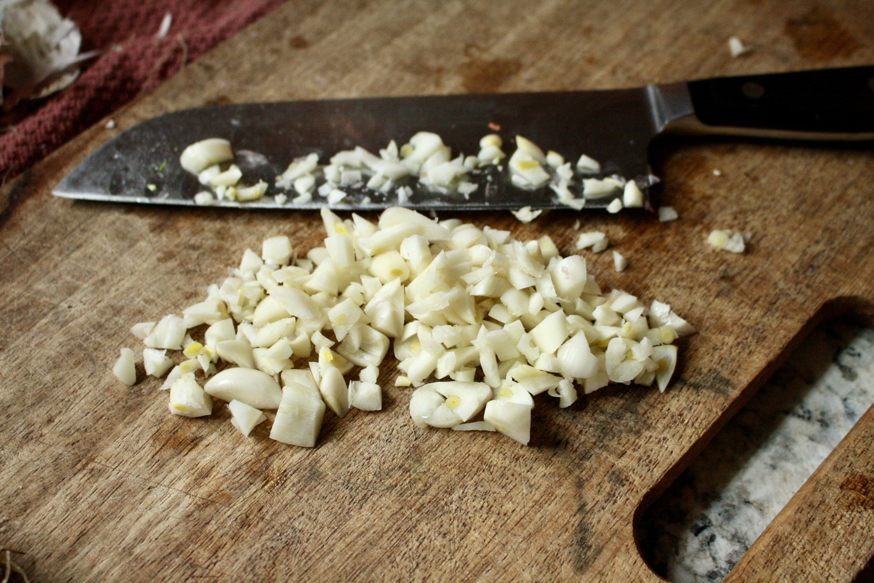 minced garlic and knife sitting on a wooden cutting board