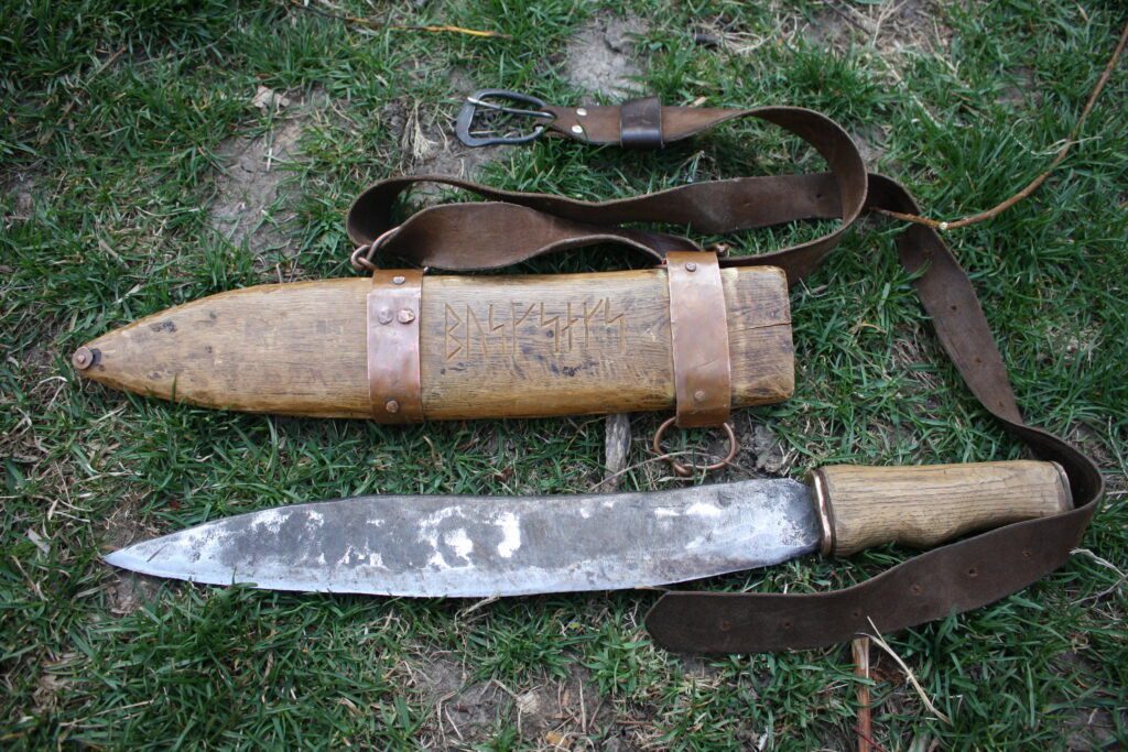 a machete knife next to a wooden sheath and leather belt on the ground