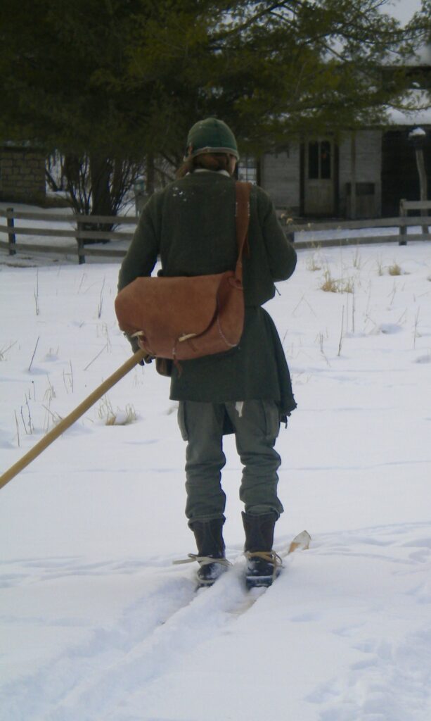 man in green tunic and leather satchel skiing in snow