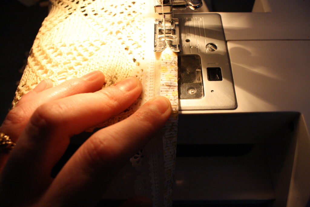 hand holding fabric while sewing lace on a sewing machine