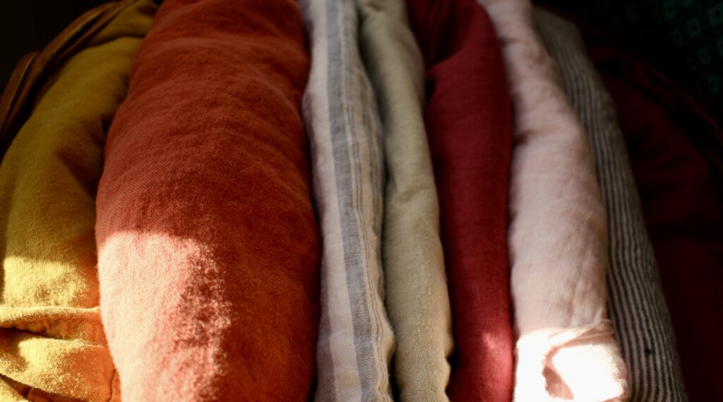 a basket with linen clothes folded next to one another. colors ranging from orange, yellow, tan, and striped