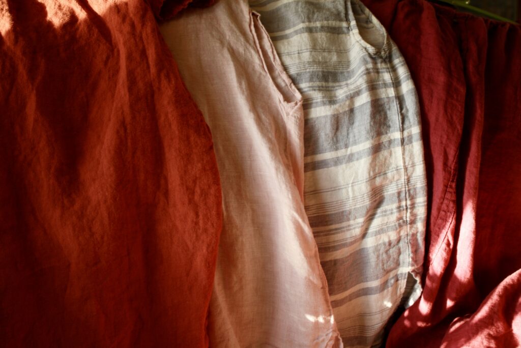 an orange, pink, blue striped, and red linen shirts lined up on hangers