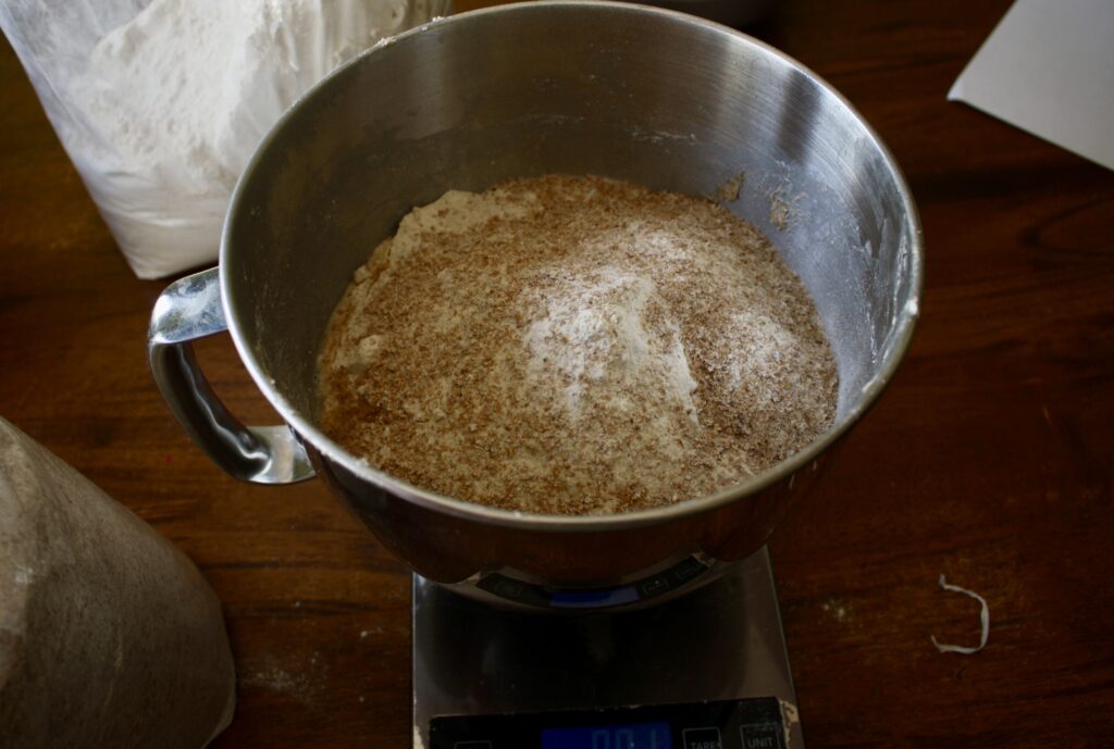 a large amount of wheat flour in a stainless steel bowl sitting on a kitchen scale