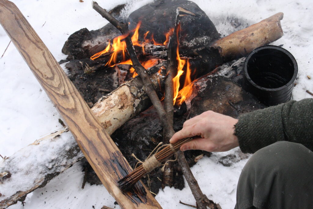 coating a wooden ski with pine tar with a brush next to a fire