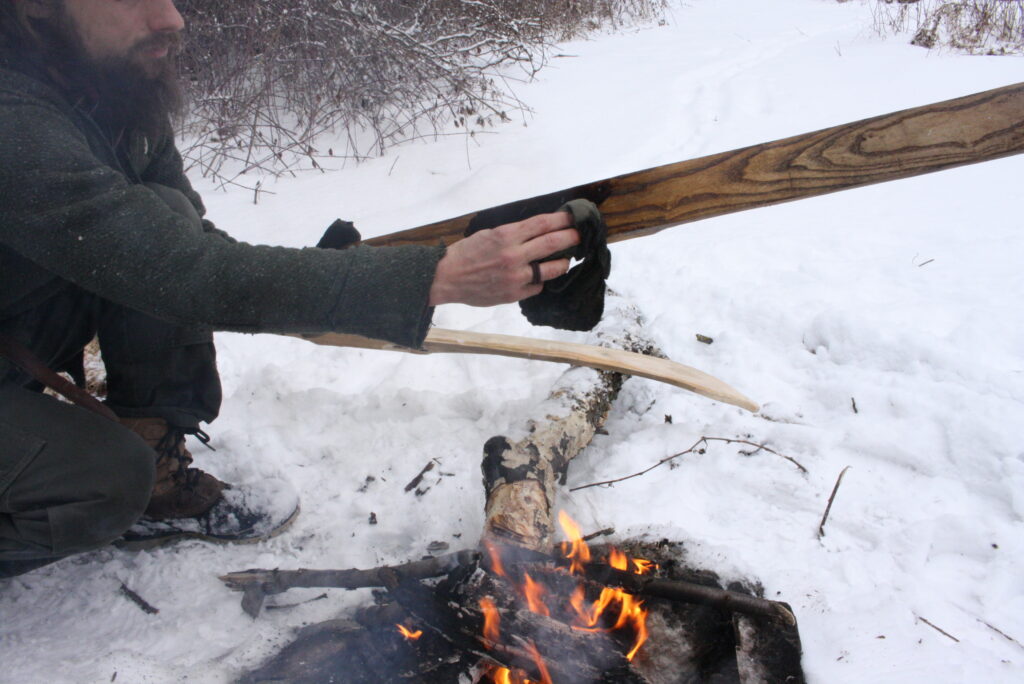 wiping on pine tar with rag on ski over a fire.  